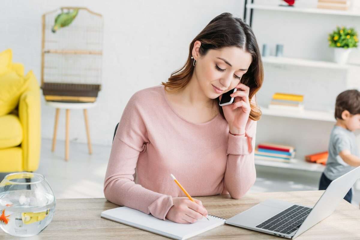 beautiful woman talking on smartphone while sitting at table with laptop at home