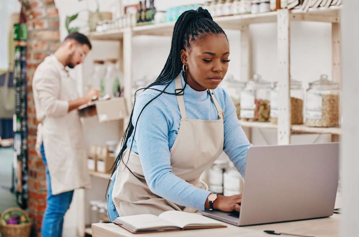 Small grocery business and black woman at counter with laptop searching for an accountant a one minute website visitor