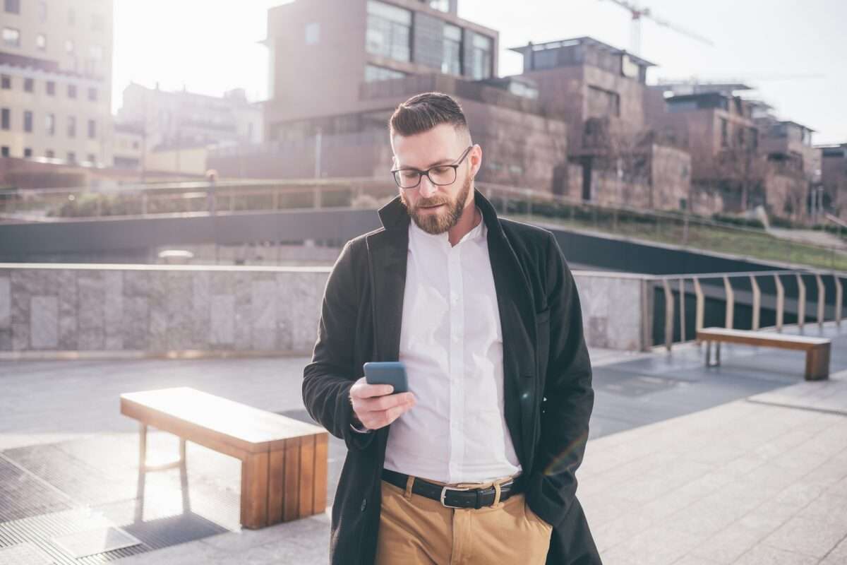Young bearded man outdoor using smartphone texting searching online buying ecommerce
